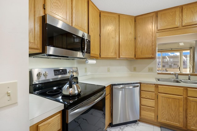 kitchen featuring marble finish floor, stainless steel appliances, a sink, and light countertops