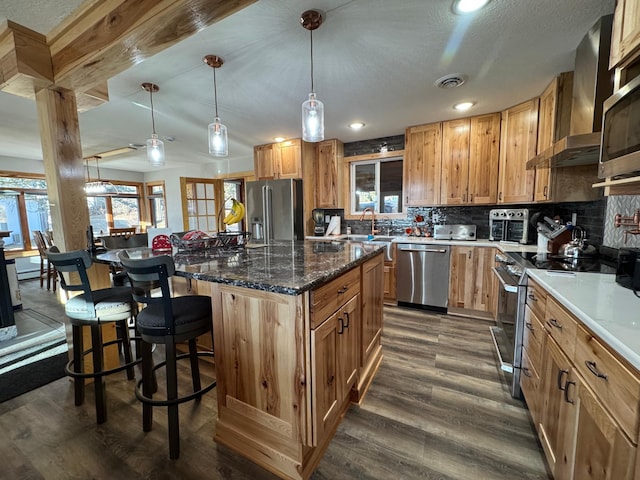 kitchen with dark wood-style floors, wall chimney exhaust hood, visible vents, appliances with stainless steel finishes, and a kitchen bar