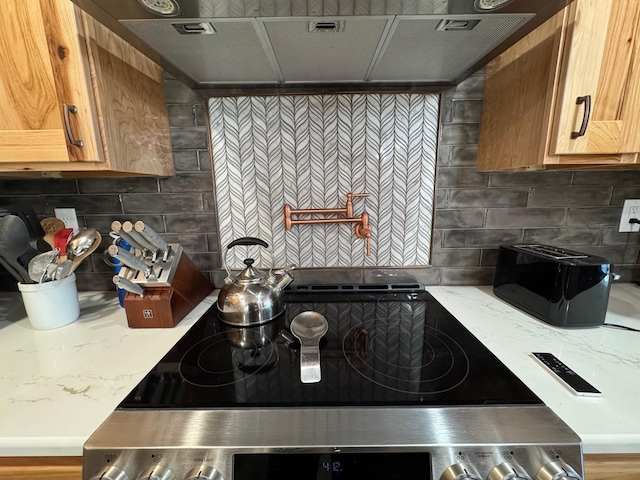 kitchen with ventilation hood, light stone counters, decorative backsplash, and stove