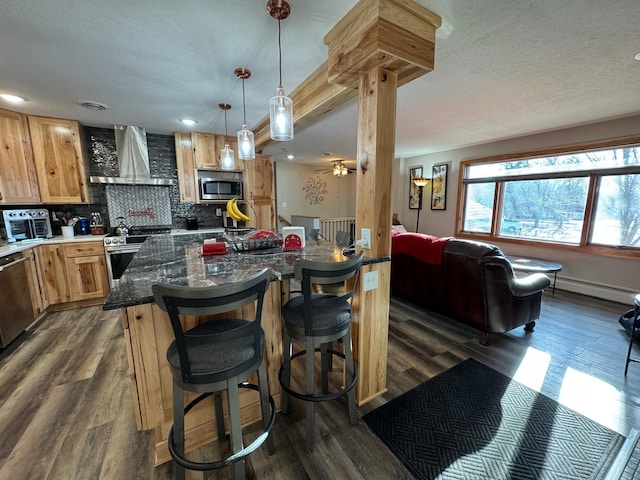 kitchen with dark wood finished floors, wall chimney exhaust hood, appliances with stainless steel finishes, a baseboard heating unit, and backsplash