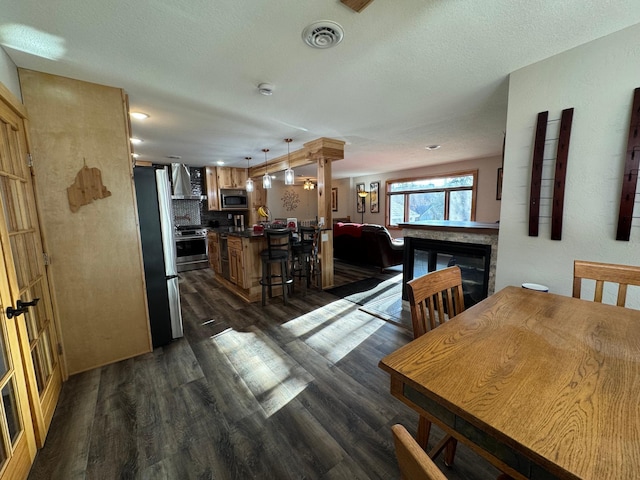 dining room featuring a glass covered fireplace, visible vents, dark wood finished floors, and a textured ceiling