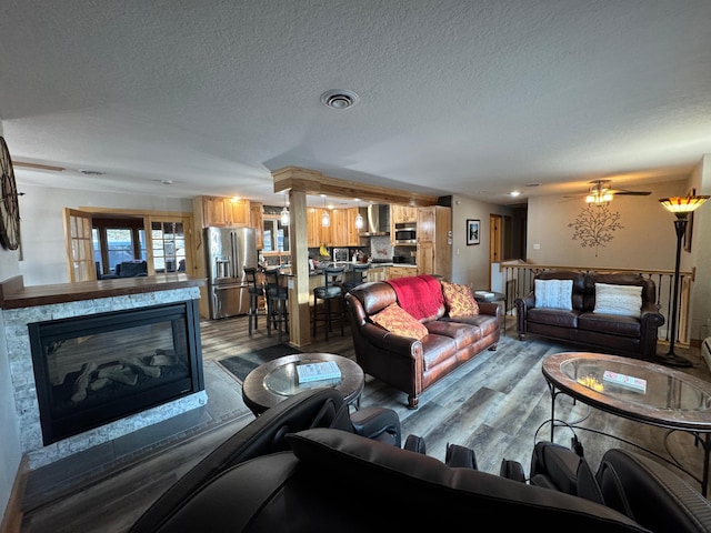 living room with a textured ceiling, a glass covered fireplace, wood finished floors, and visible vents