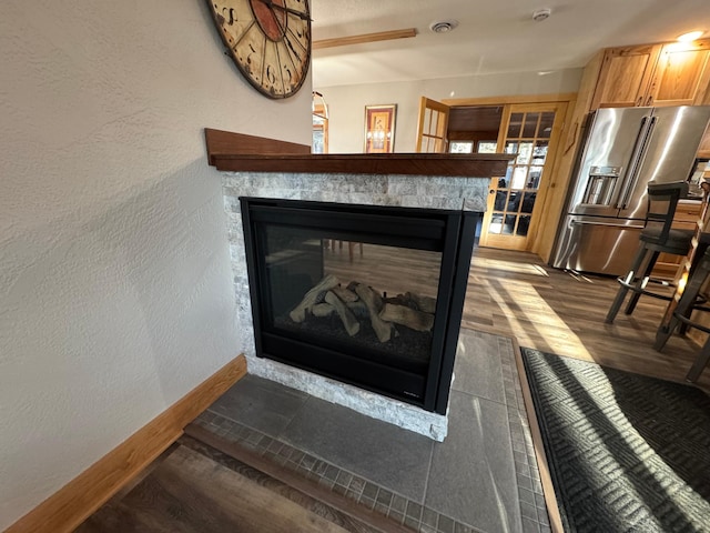 interior details with baseboards, a textured wall, high quality fridge, wood finished floors, and a multi sided fireplace