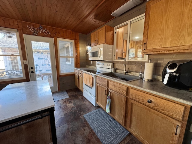 kitchen with wooden walls, white appliances, a sink, wood ceiling, and light countertops