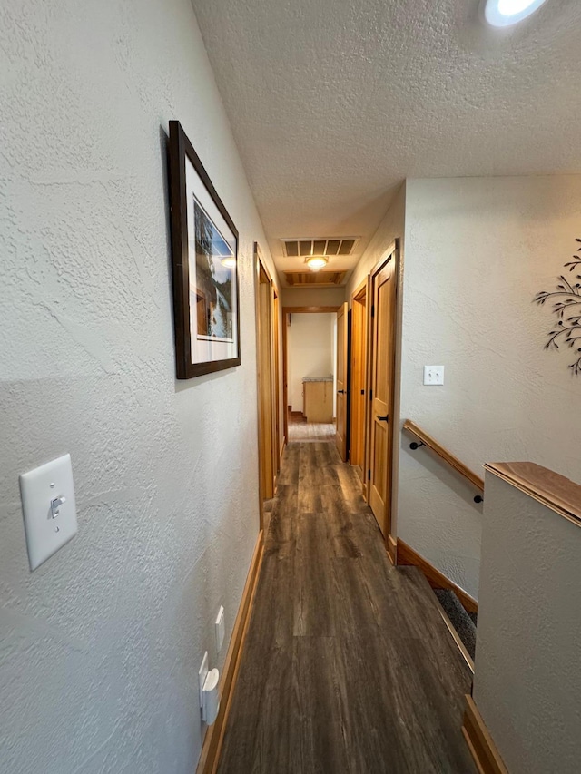 hall featuring visible vents, baseboards, dark wood finished floors, a textured wall, and a textured ceiling