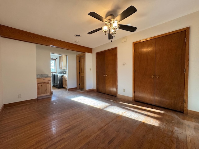 unfurnished bedroom featuring ceiling fan, visible vents, baseboards, wood-type flooring, and two closets