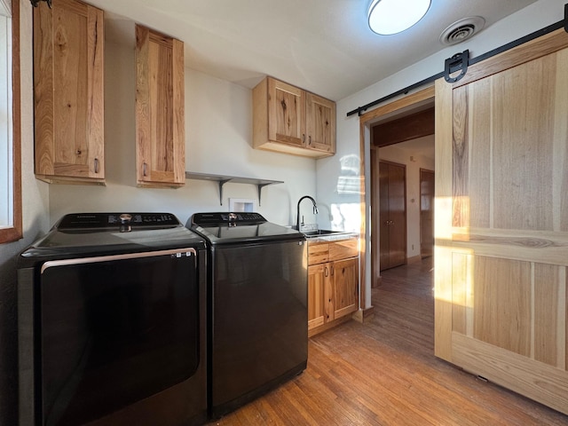 washroom with a barn door, washing machine and dryer, a sink, visible vents, and light wood finished floors