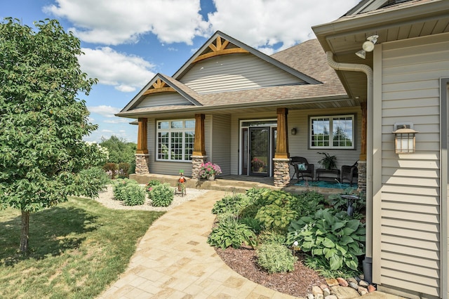 view of exterior entry featuring a porch and a shingled roof