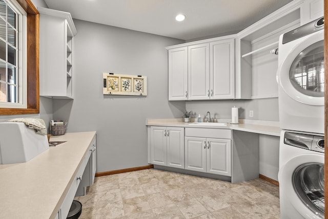 laundry area featuring stacked washer / drying machine, recessed lighting, cabinet space, a sink, and baseboards