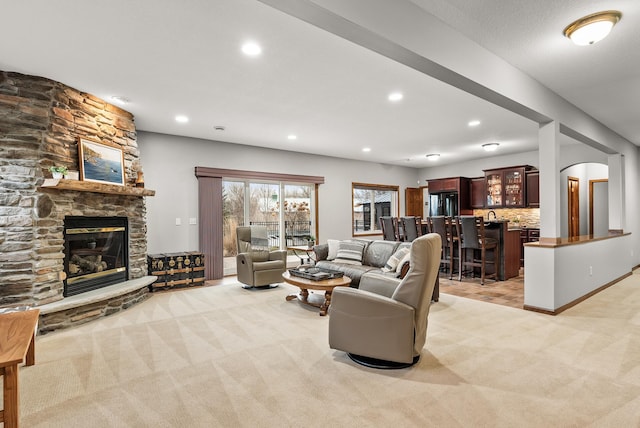 living area featuring arched walkways, a stone fireplace, recessed lighting, light colored carpet, and baseboards