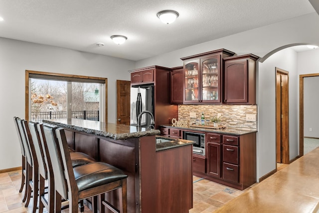 kitchen with arched walkways, decorative backsplash, freestanding refrigerator, built in microwave, and a sink