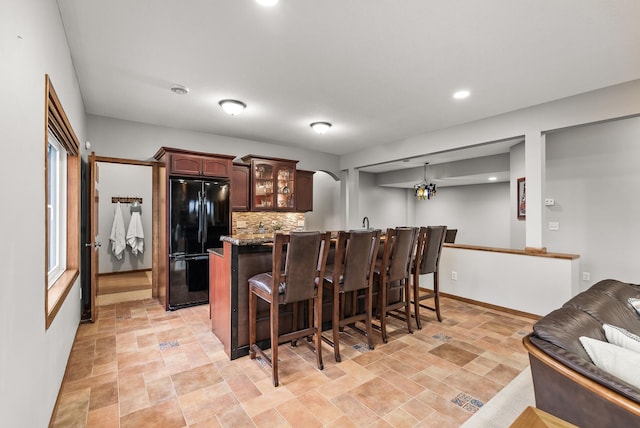 kitchen featuring dark brown cabinetry, a breakfast bar, freestanding refrigerator, tasteful backsplash, and glass insert cabinets