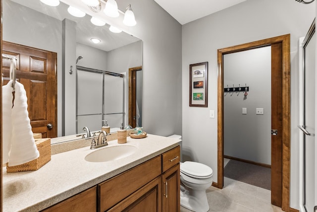 full bathroom featuring toilet, a shower with shower door, vanity, baseboards, and tile patterned floors