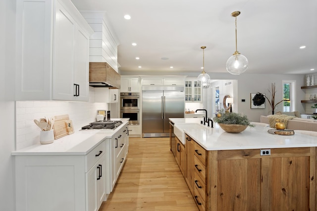 kitchen with white cabinets, decorative backsplash, appliances with stainless steel finishes, light wood-style floors, and a sink