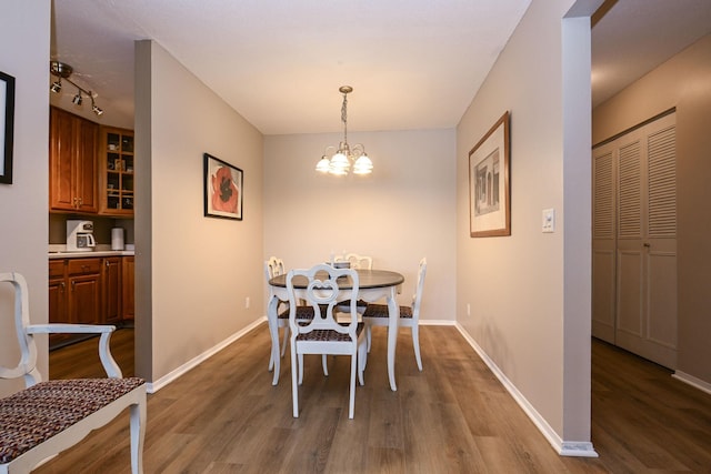 dining space featuring track lighting, dark wood finished floors, baseboards, and an inviting chandelier