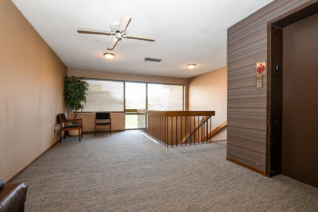 unfurnished room featuring visible vents, elevator, an upstairs landing, a textured ceiling, and carpet flooring