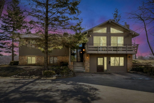 view of front of property featuring driveway, brick siding, a chimney, and a balcony