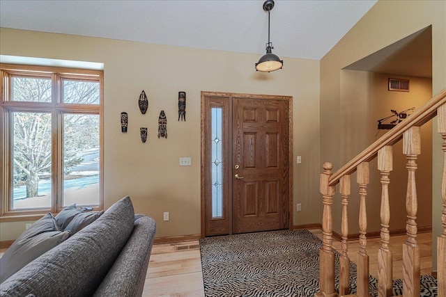 foyer featuring lofted ceiling, visible vents, light wood-style flooring, baseboards, and stairs