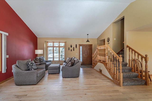 living area with stairs, high vaulted ceiling, and wood finished floors