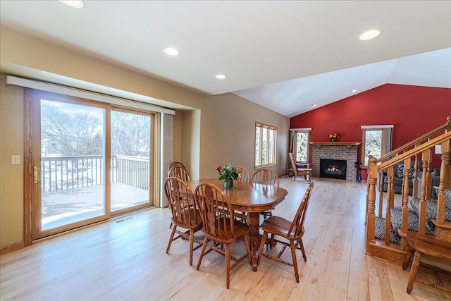 dining space featuring lofted ceiling, recessed lighting, a fireplace, light wood-style floors, and stairway