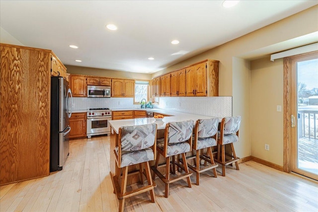 kitchen with a peninsula, a sink, appliances with stainless steel finishes, light wood-type flooring, and tasteful backsplash