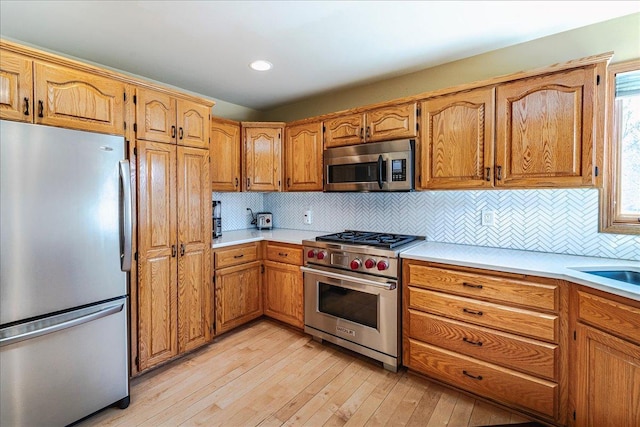 kitchen with appliances with stainless steel finishes, brown cabinetry, light countertops, and light wood-style floors