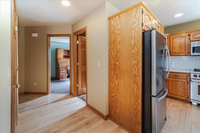 kitchen with appliances with stainless steel finishes, light wood-style floors, baseboards, and tasteful backsplash