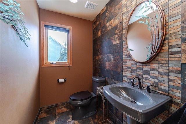 bathroom featuring toilet, a sink, visible vents, baseboards, and stone tile flooring