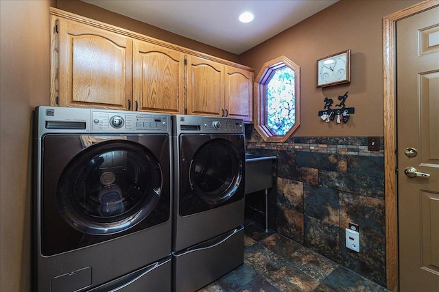 clothes washing area featuring tile walls, washer and dryer, wainscoting, cabinet space, and stone finish flooring