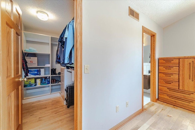 hall with light wood-type flooring, visible vents, and a textured ceiling