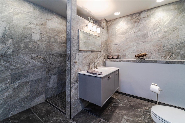 bathroom featuring toilet, a walk in shower, tile walls, and vanity