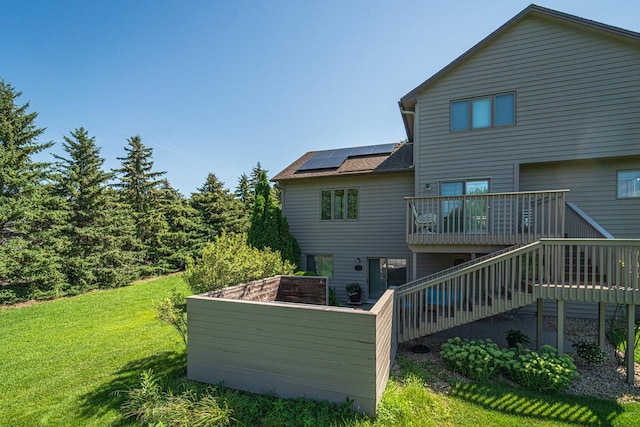 rear view of property with stairs, a yard, a wooden deck, and roof mounted solar panels