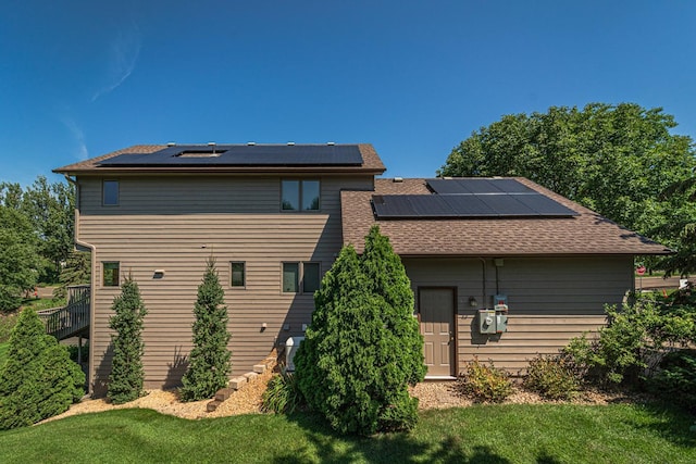 rear view of property featuring roof with shingles, roof mounted solar panels, and a yard