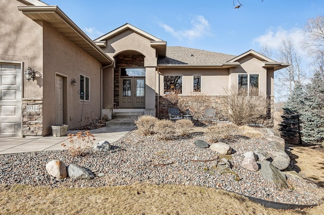 view of front of home with a garage, stone siding, french doors, and stucco siding