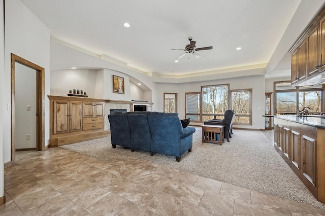 living area with light carpet, a tray ceiling, a fireplace, and baseboards