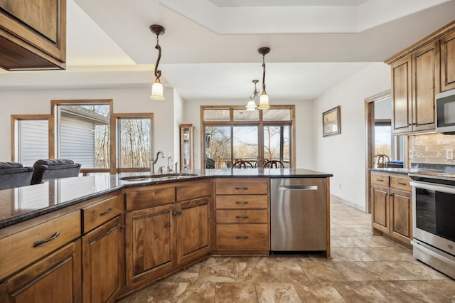 kitchen with tasteful backsplash, dark stone countertops, decorative light fixtures, stainless steel appliances, and a sink