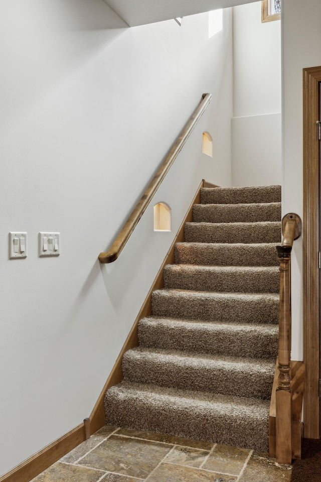 staircase featuring stone finish floor and baseboards