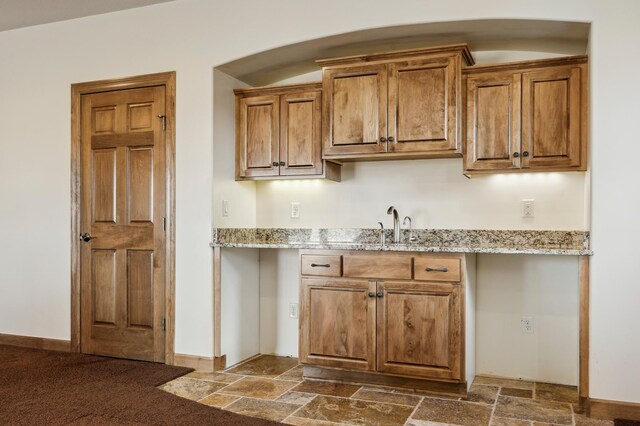 kitchen with light stone countertops, stone tile floors, brown cabinetry, and a sink