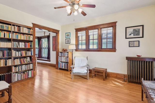 sitting room featuring a ceiling fan, light wood-type flooring, radiator, and baseboards