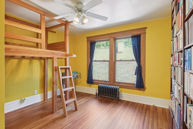 bedroom featuring baseboards, hardwood / wood-style floors, a ceiling fan, and radiator