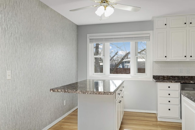 kitchen featuring light wood finished floors, baseboards, white cabinets, and dark stone countertops