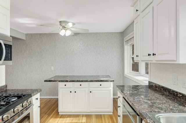 kitchen with light wood-style flooring, stainless steel appliances, white cabinetry, dark stone countertops, and wallpapered walls