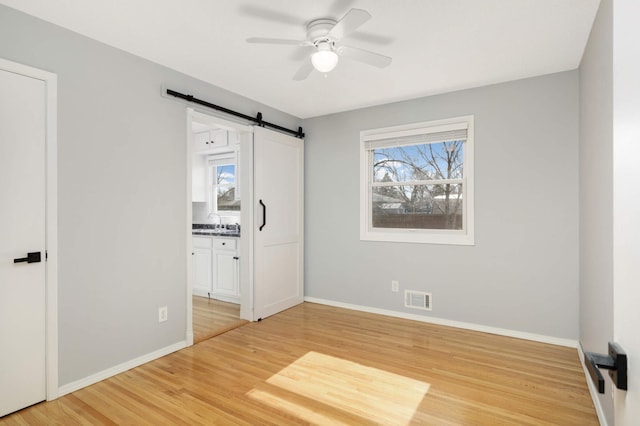 unfurnished bedroom with light wood finished floors, visible vents, a barn door, a sink, and baseboards