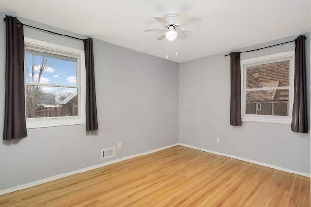 spare room with a ceiling fan, visible vents, baseboards, and wood finished floors