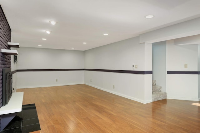 unfurnished living room with light wood-style floors, recessed lighting, a brick fireplace, and stairway