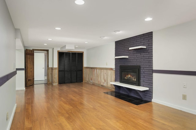 unfurnished living room featuring recessed lighting, a brick fireplace, a wainscoted wall, and wood finished floors