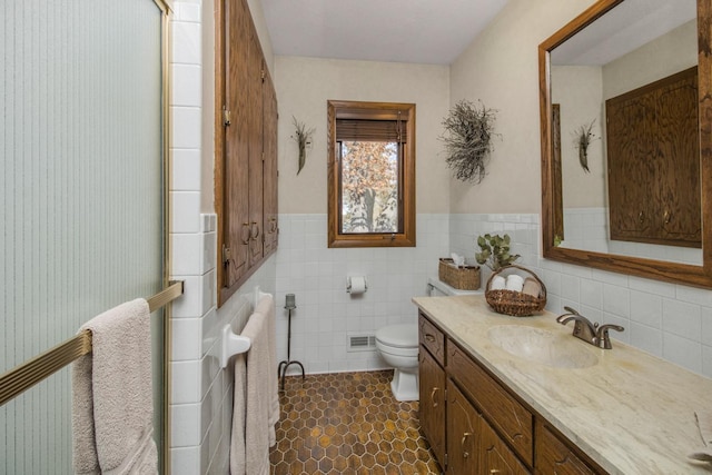 bathroom featuring toilet, a wainscoted wall, vanity, visible vents, and tile walls