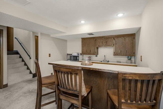 kitchen with light carpet, light countertops, a breakfast bar, and a sink