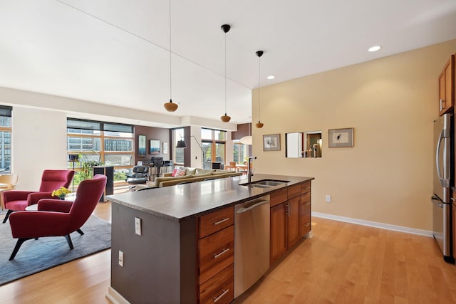 kitchen with light wood finished floors, dark countertops, appliances with stainless steel finishes, brown cabinetry, and a sink