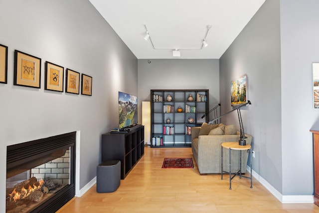 sitting room with track lighting, a warm lit fireplace, baseboards, and wood finished floors